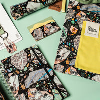 Collection of patterned products including notebooks, keychains, and pouches on a green background.