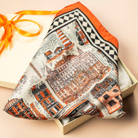 Silk scarf with architectural illustrations and an orange border in a box with an orange ribbon