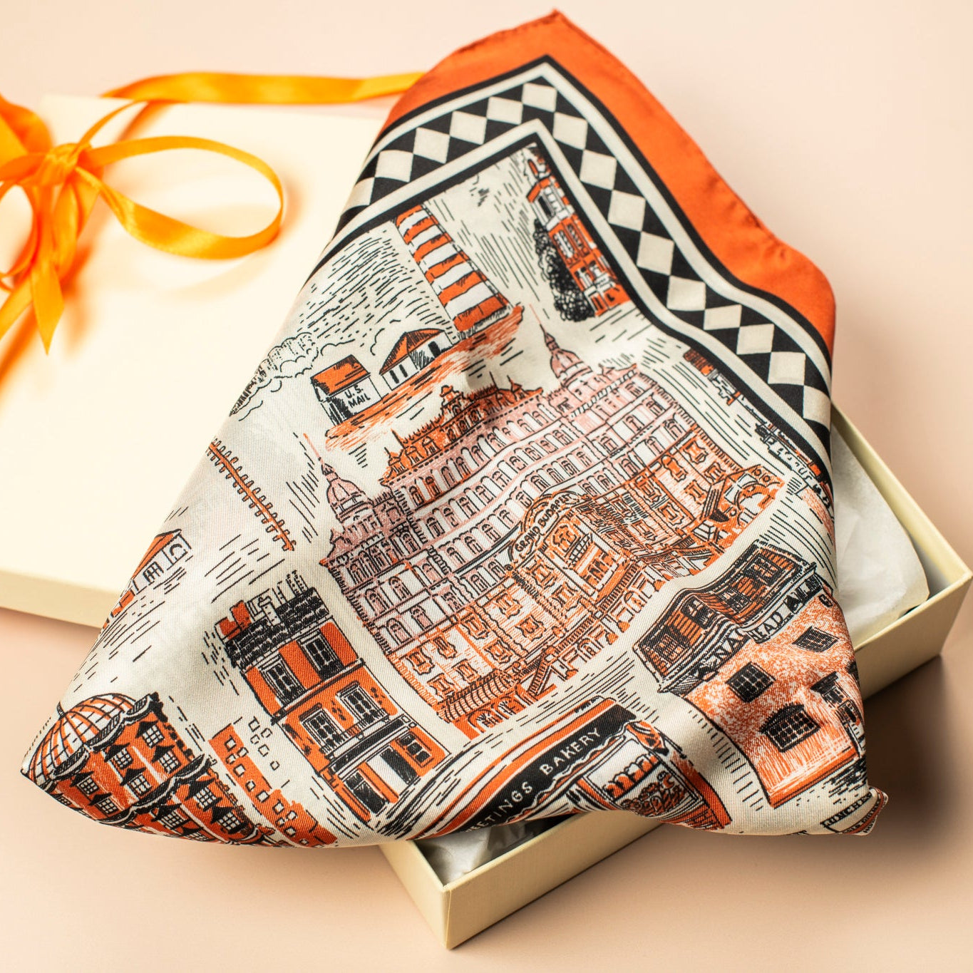 Silk scarf with architectural illustrations and an orange border in a box with an orange ribbon