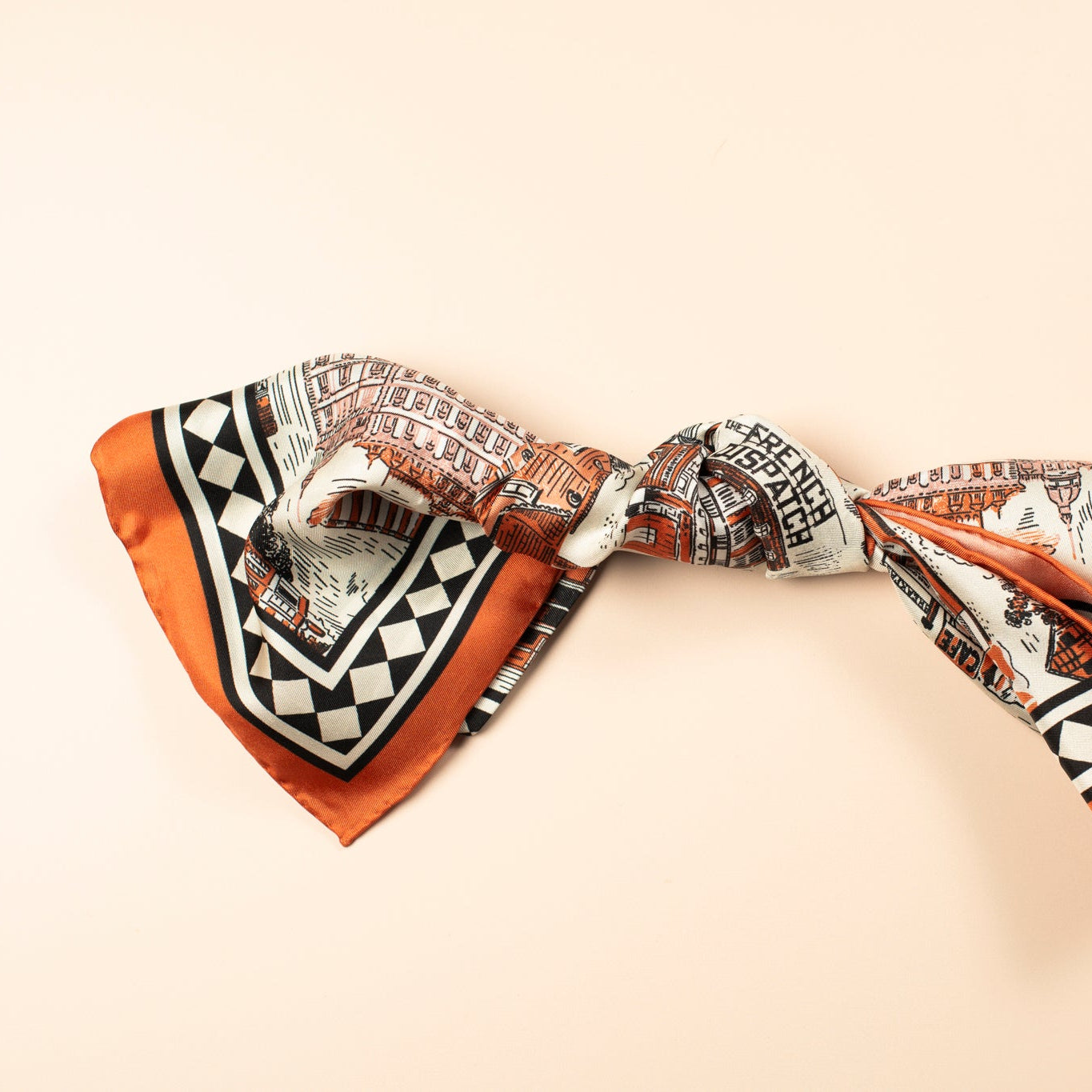 Scarf with orange and black architectural illustrations tied in a knot on a beige background