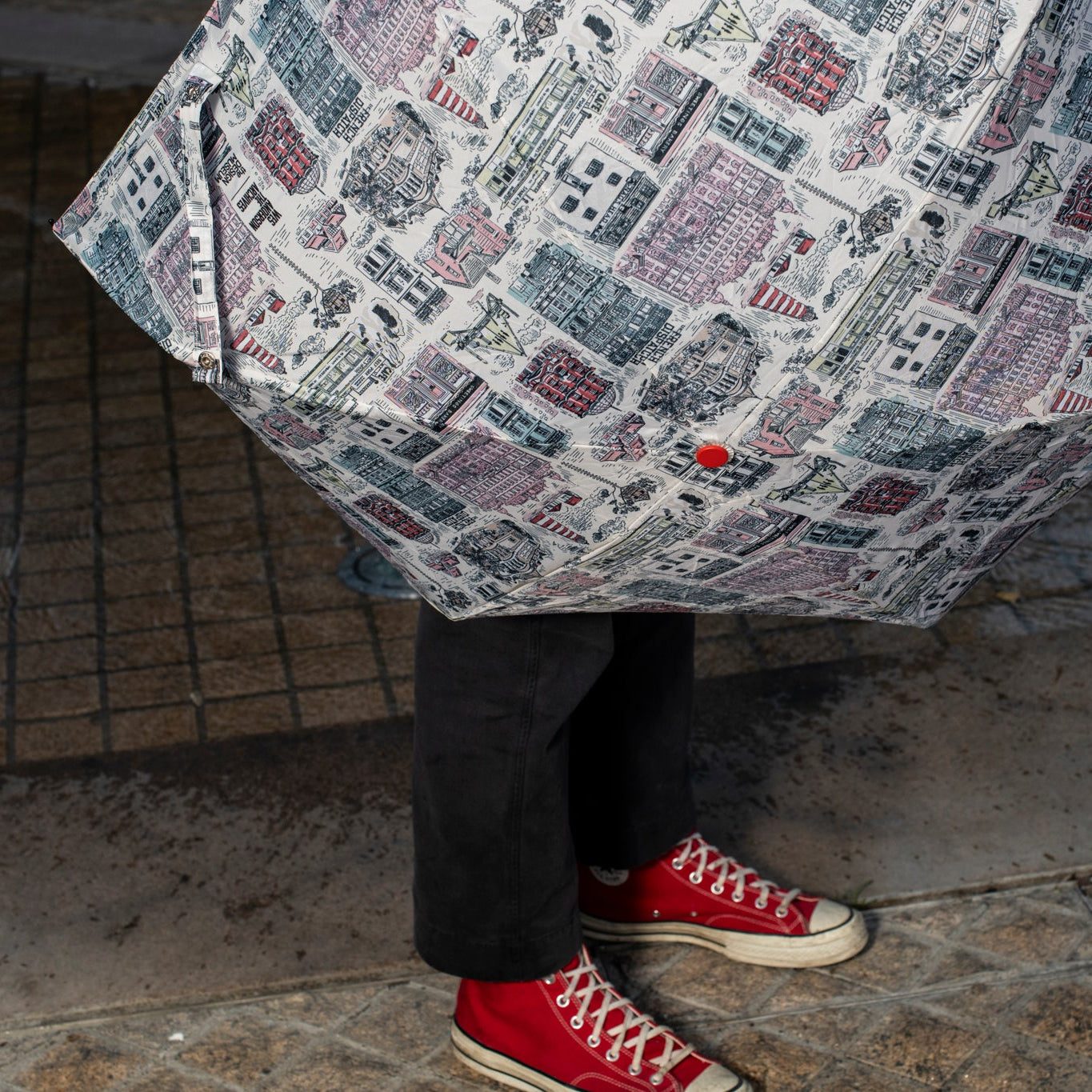 Person holding a white umbrella with building illustrations on a stone pavement