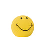 A cordless, round lamp with a yellow silicone body and a smiling face design.