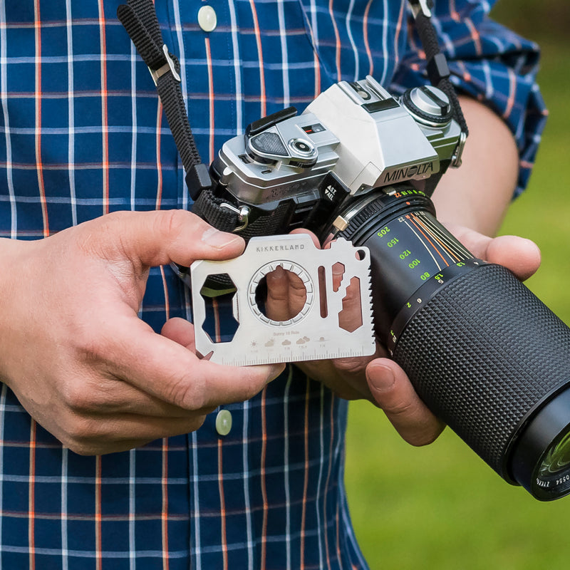A person holding a silver steel camera multi tool next to a camera.