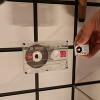 Person holding a cassette tape against a tiled wall with a grid pattern