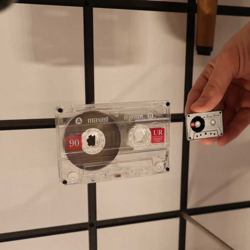Person holding a cassette tape against a tiled wall with a grid pattern
