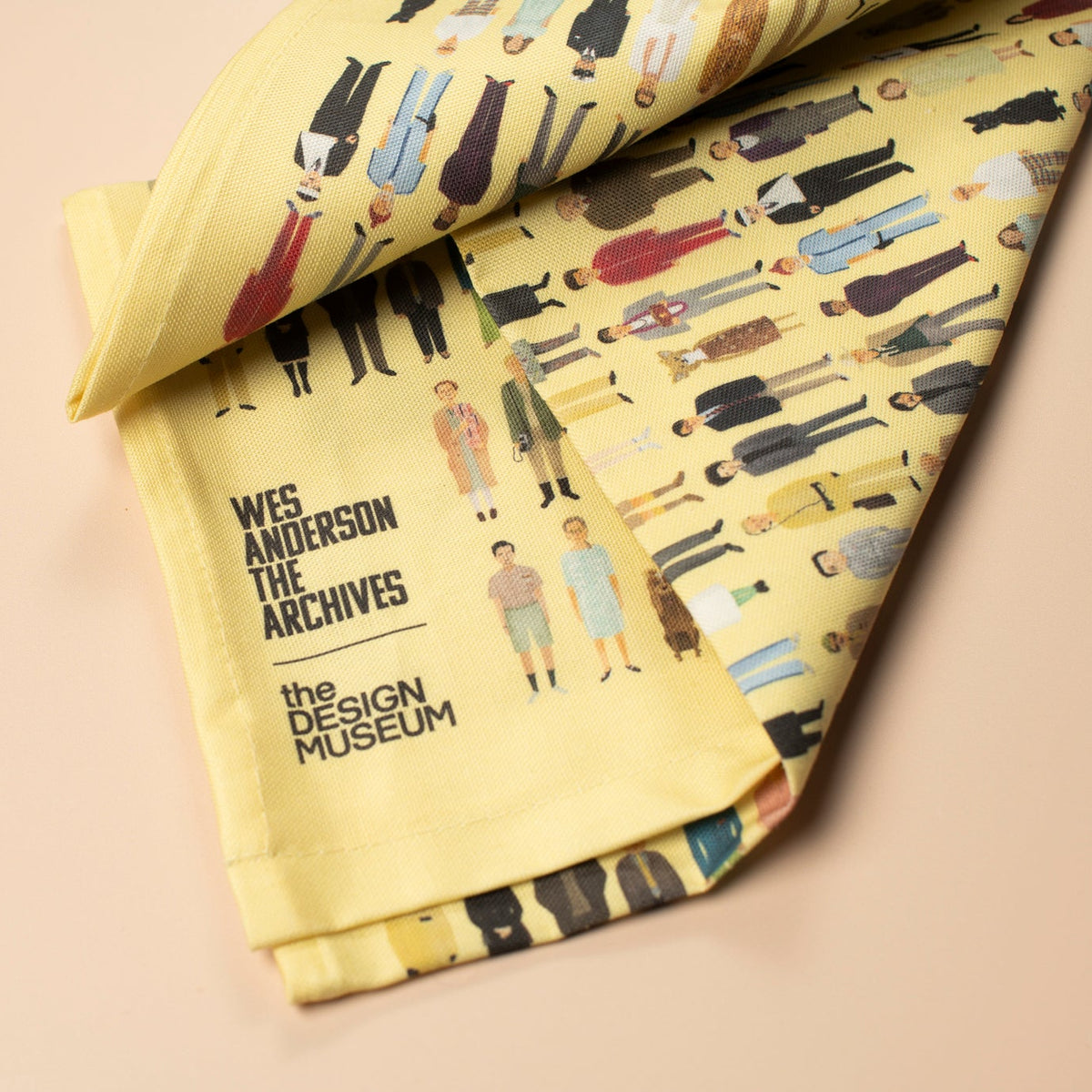 Yellow tea towel with a pattern of illustrated figures on a light pink background.