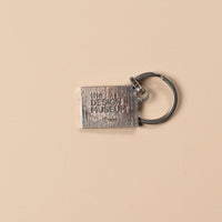 Silver rectangular keychain with 'The Design Museum' branding on a beige background