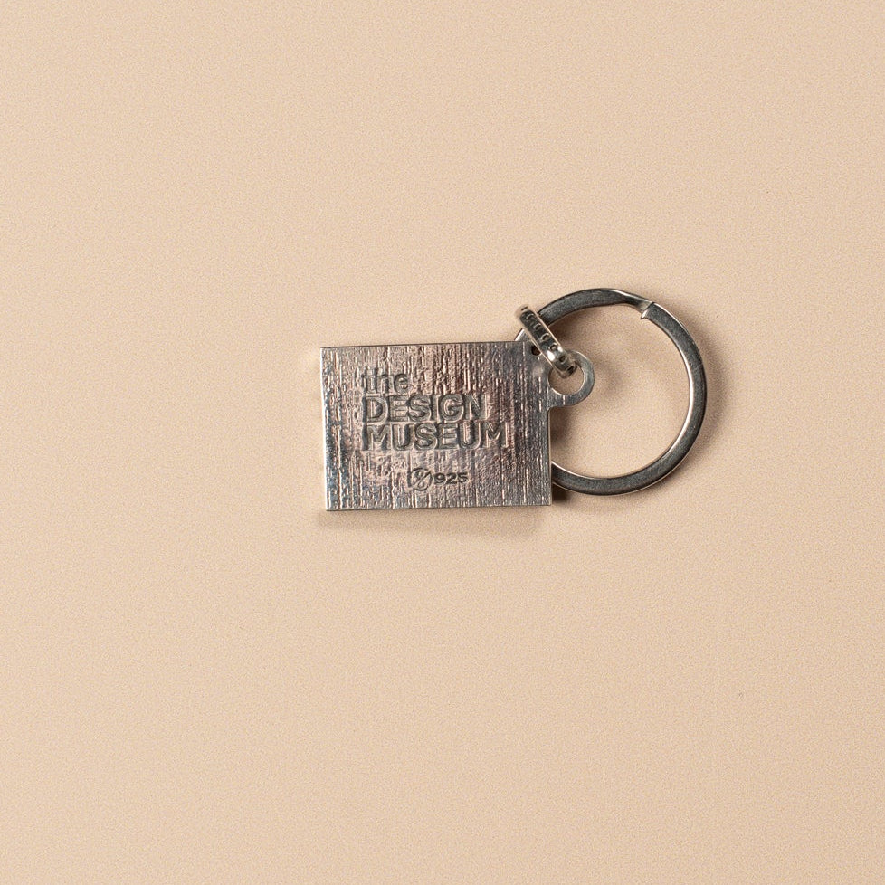 Silver rectangular keychain with 'The Design Museum' branding on a beige background