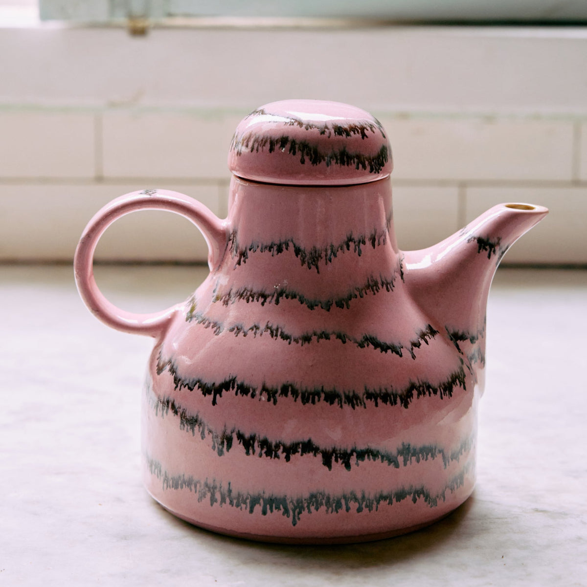 A pink and black abstract ceramic coffee pot on a white surface.
