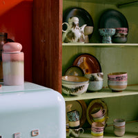 Vintage-style kitchen with a retro refrigerator and wooden shelf displaying ceramic items against an orange wall.
