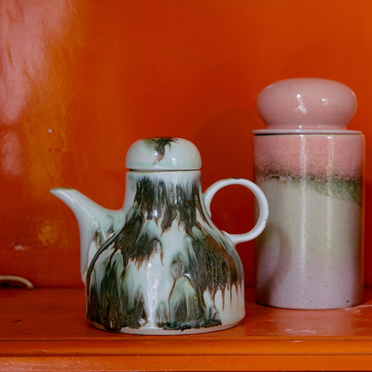 Colourful abstract ceramic pieces on an orange shelf.