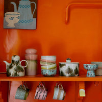 Colourful ceramic hand-painted pieces on an orange shelf