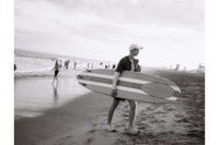 Person carrying a surfboard on a beach with other people in the background