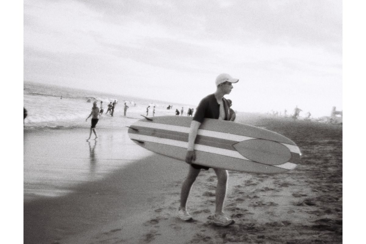 Person carrying a surfboard on a beach with other people in the background