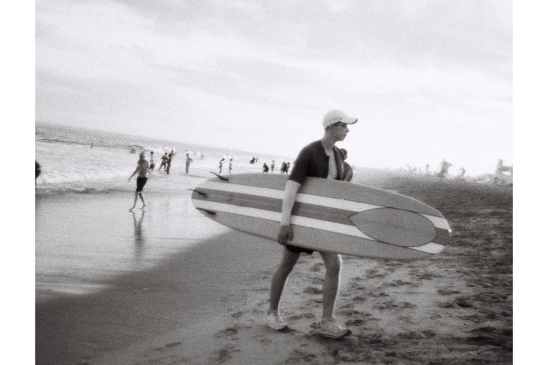 Person carrying a surfboard on a beach with other people in the background