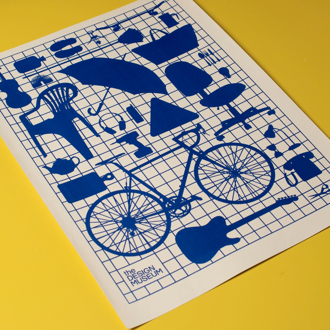 A white monochrome screen print featuring blue everyday objects on a blue grid laid flat on a yellow background