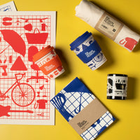 Collection of design museum branded products including cups, notebooks, and a poster on a yellow background.