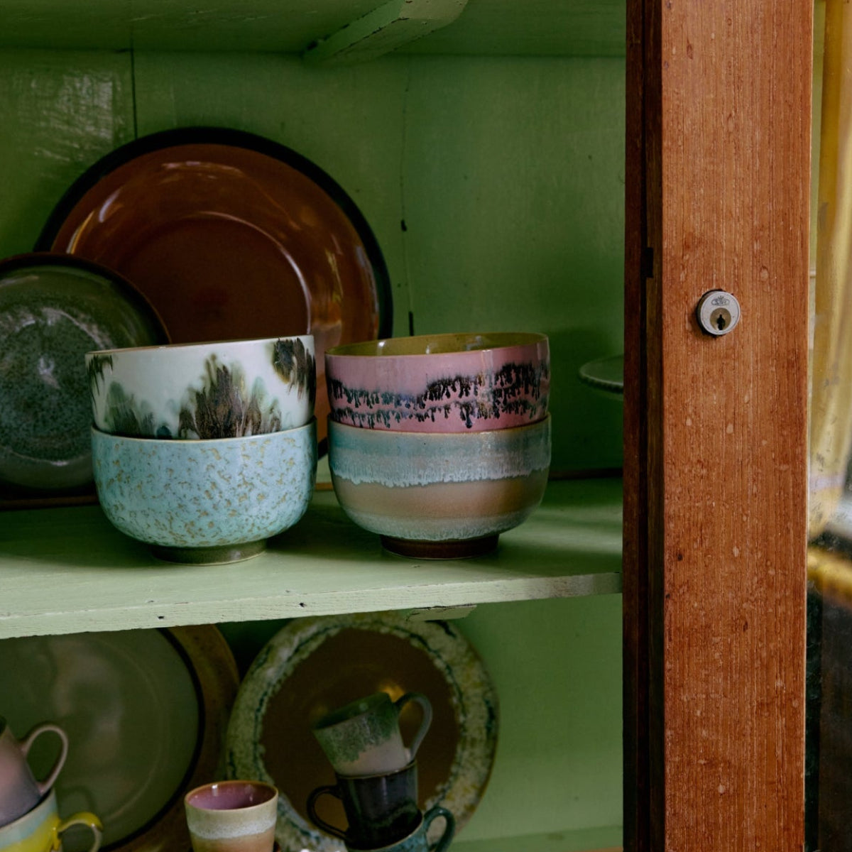 Colourful absract ceramic bowls and cups inside a green cupboard.