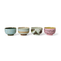 A set of 4 colourful abstract hand-painted ceramic noodle bowls in a row on a white background. 