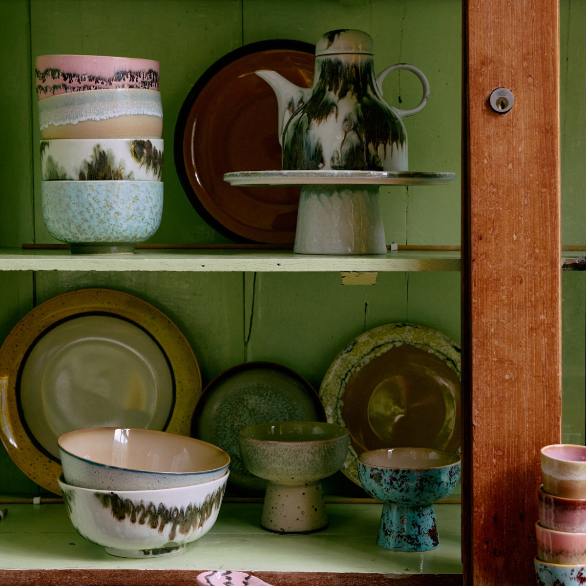 Colourful absract ceramic bowls and stoneware inside a green cupboard.