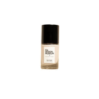 A bottle of off white nail polish by The Design Museum, featuring a black cap and a white label, set against a solid cream-colored background.