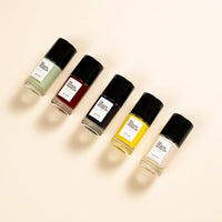 Five bottles of nail polish arranged diagonally on a warm cream background. 