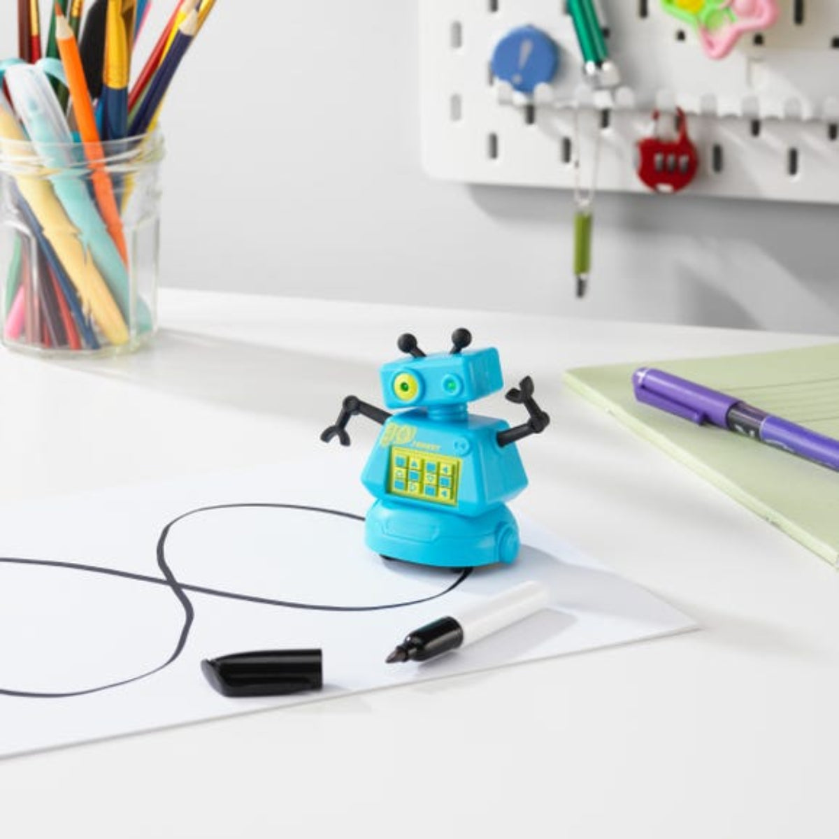 Toy robot on a desk with markers and stationery items in the background