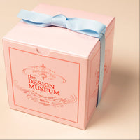 Pink Mendl's teabags box with a blue ribbon from the Design Museum on a beige background