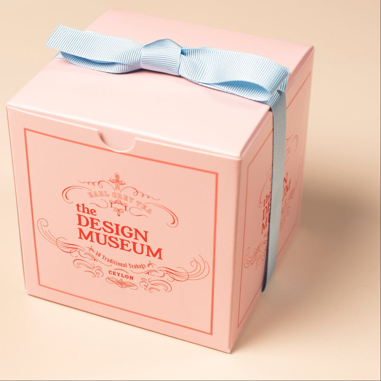 Pink Mendl's teabags box with a blue ribbon from the Design Museum on a beige background