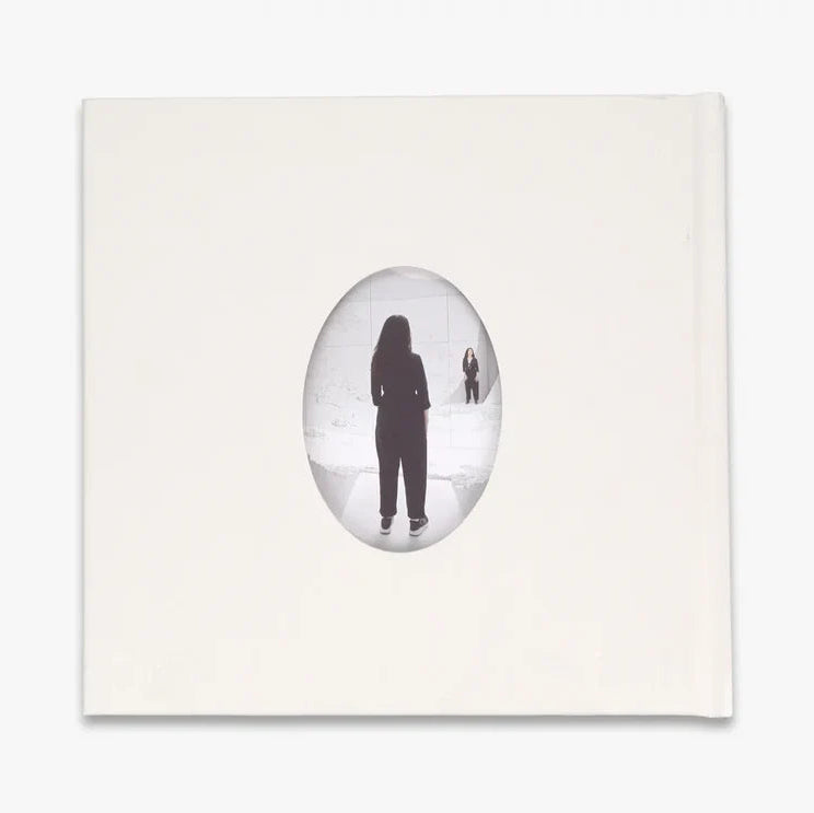 The back of a white book featuring a central oval frame containing a black silhouette of a person standing in a snowy white landscape, set against a clean white background.