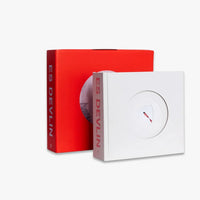 A square white album-style box in the foreground with a circular cutout and a small red-and-white object inside, positioned in front of a tall red box. The visible text reads 'ES DEVILIN' on both boxes.