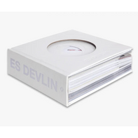 A white hardcover book with a circular cutout on the cover, shown at an angle on a light gray background. The side of the book displays the text 'ES DEVLIN' in a light gray font.