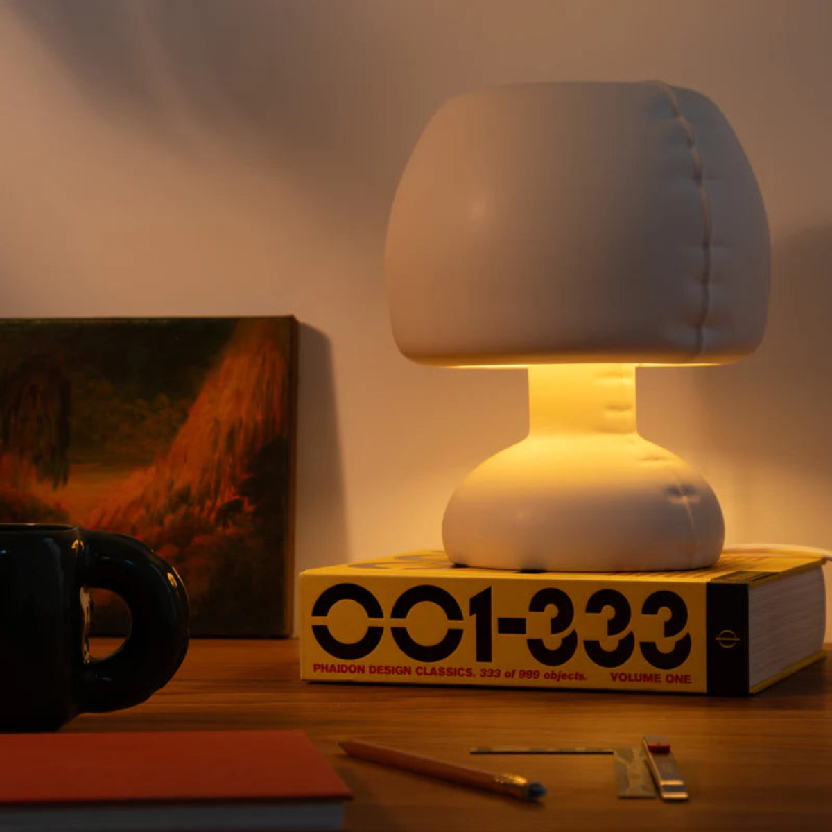 White lamp on a book with a mug, notebook, and pencil on a wooden surface.