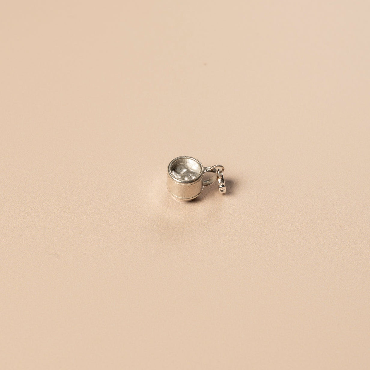 Small silver teacup charm on a beige background