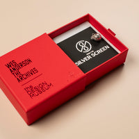 Red jewellery box with a black card and a silver charm featuring 'The Design Museum' logo on a beige background