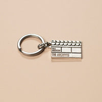 Silver clapperboard keychain on a beige background