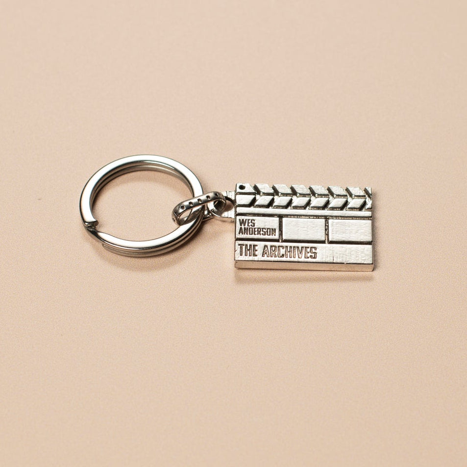 Silver clapperboard keychain on a beige background