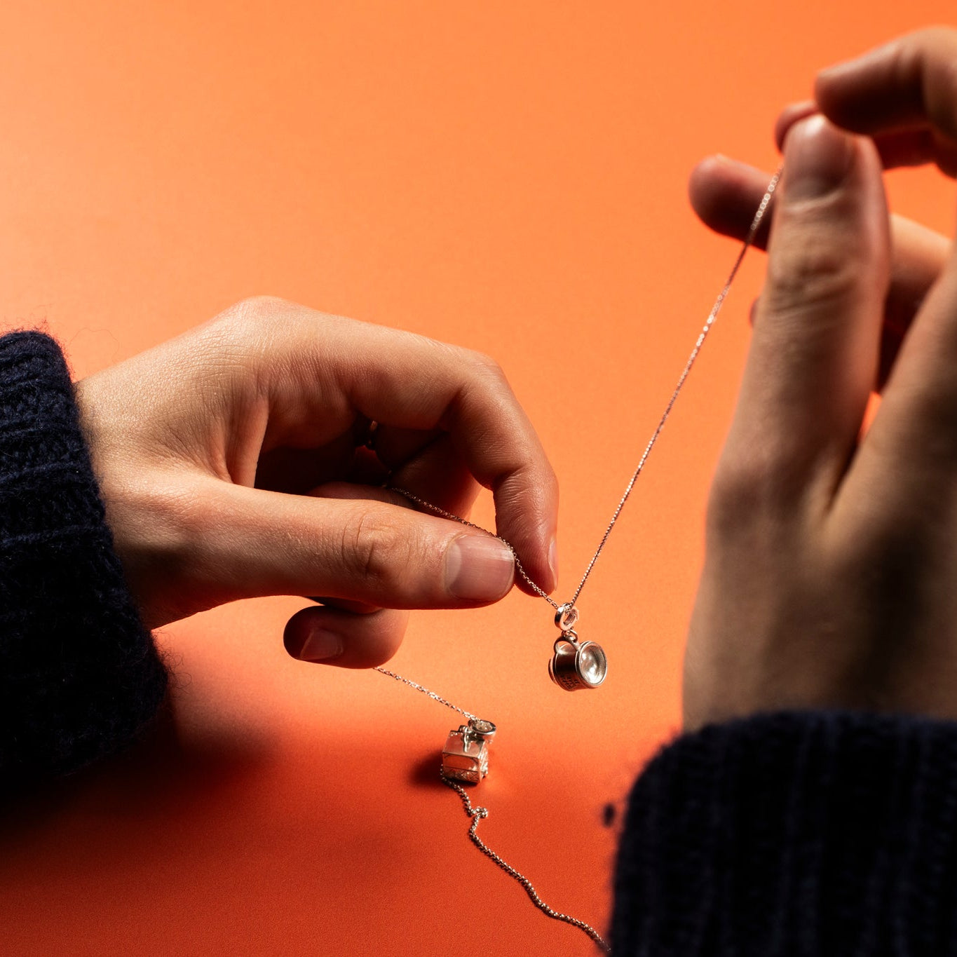 Close-up of hands holding a silver necklace with charms against an orange background