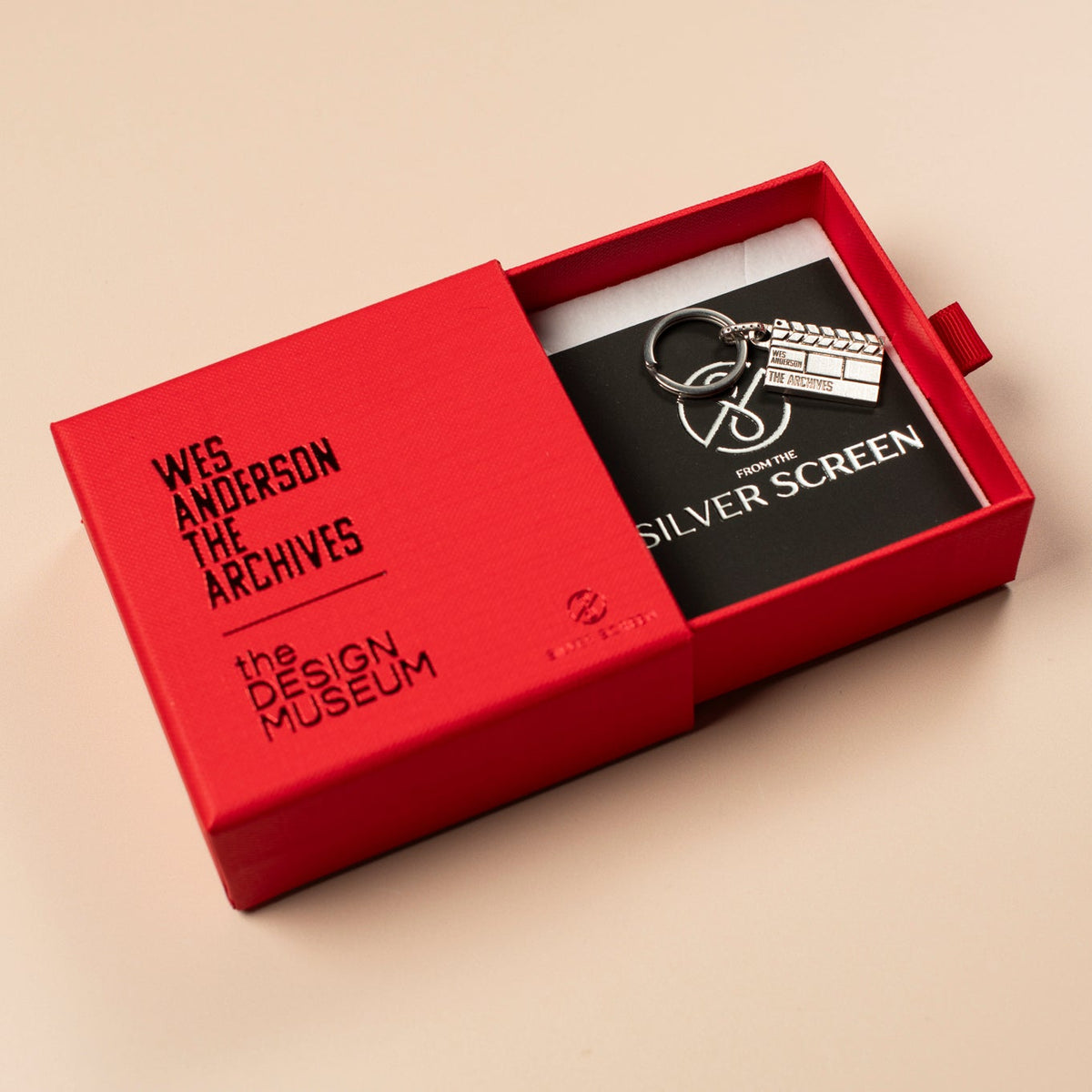 Red jewellery box with a silver clapperboard keychain inside on a beige background 