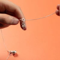 Close-up of hands holding a silver necklace with a seahorse charm against an orange background