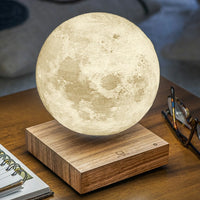 Moon lamp on a wooden base with a notebook, pen, and glasses in the background