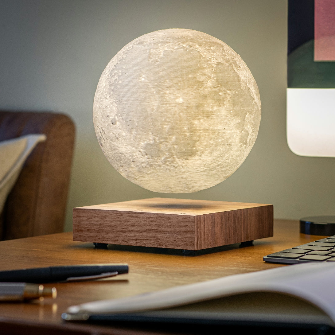 Levitating moon lamp with a wooden base on a table with books and pens.