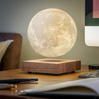 Levitating moon lamp with a wooden base on a table with books and pens.