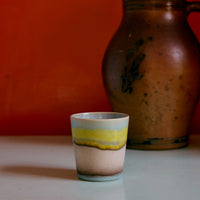 A colourful abstract ceramic mug on a white surface against an orange wall.