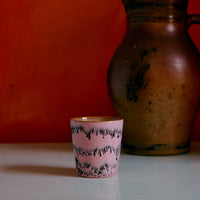 A colourful abstract ceramic mug on a white surface against an orange wall.