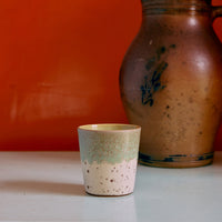A colourful abstract ceramic mug on a white surface against an orange wall.