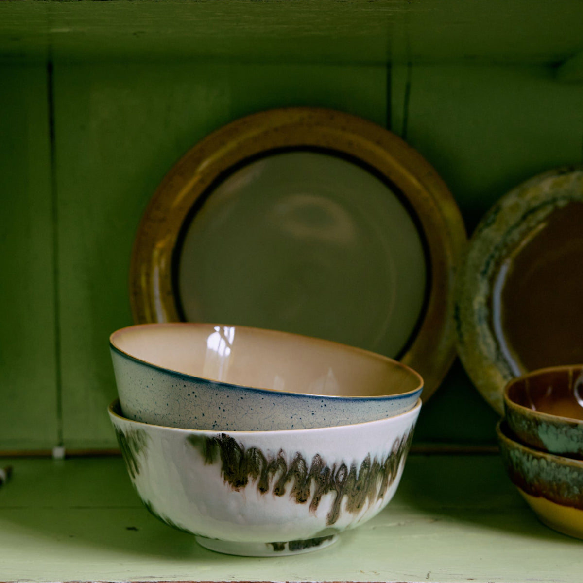 Two green and blue abstract ceramic bowls stacked inside a green cupboard.