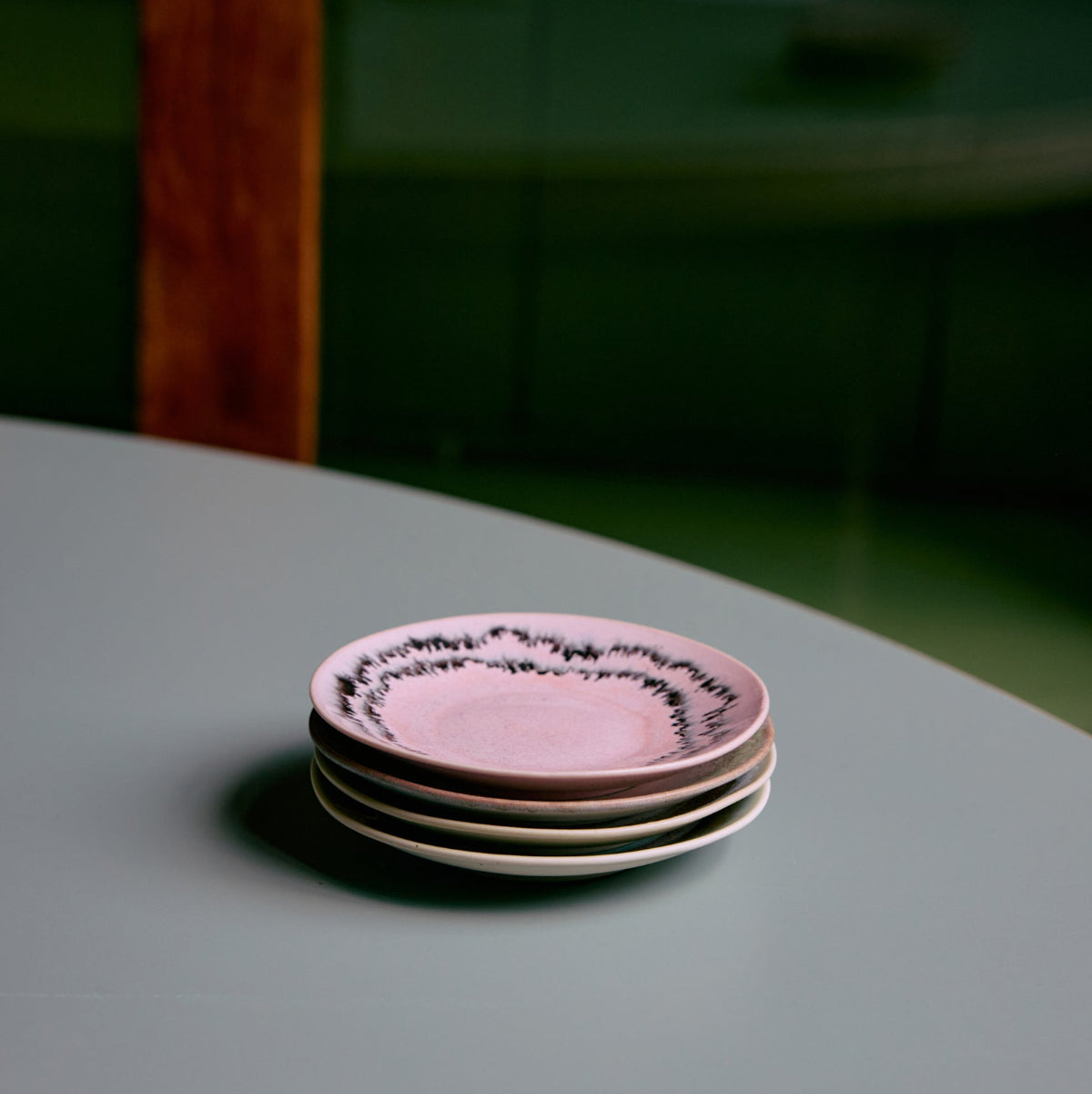 Stack of pink ceramic saucers on a green surface with a wooden bench in the background