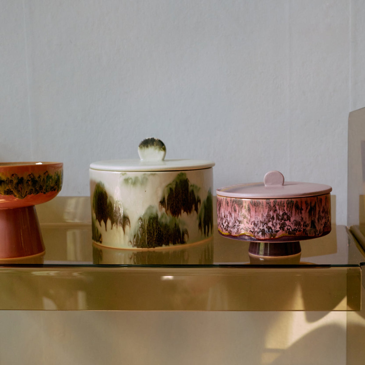A collection of colourful abstract ceramic jars and cups on a gold shelf.