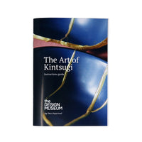 Kintsugi instructions booklet with the title 'The Art of Kintsugi' on the background of a blue plate with gold kinstugi mending.